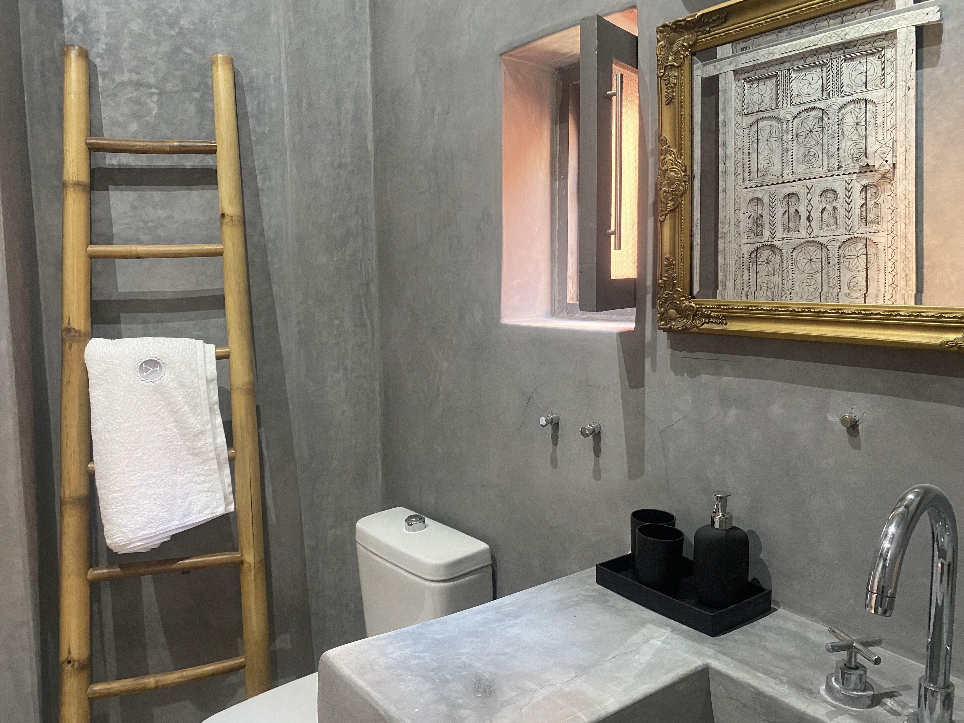 Une salle de bain avec une échelle en bois, des toilettes, un lavabo avec un robinet et une œuvre d’art encadrée accrochée au mur.