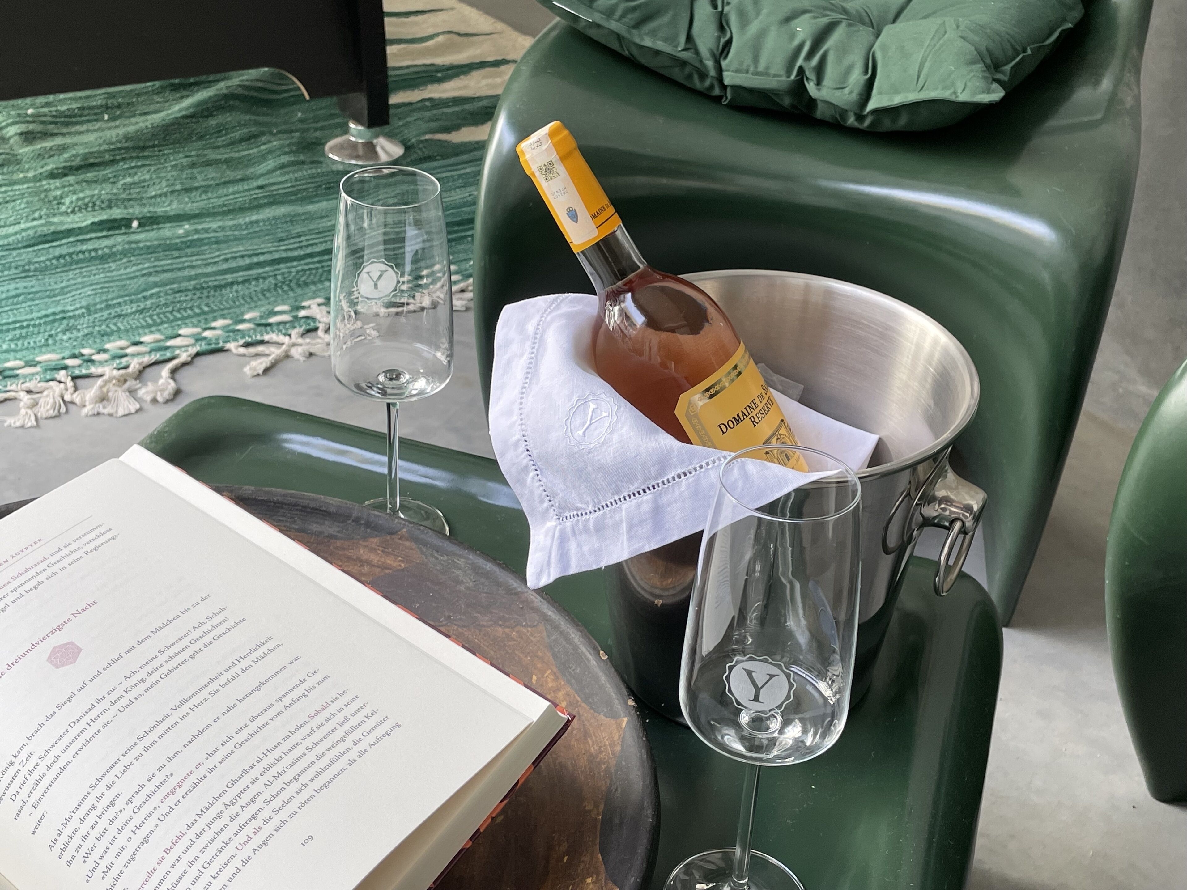 A green chair with a bottle of Domaine de la Salle Reserve wine and two empty wine glasses on a table.