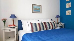 A neatly arranged hotel room with a bed, two bedside tables, a nightstand, a framed picture on the wall, and a blue wall with posters. - Little Broggi - 15mins walking from Central Station. (Milano)