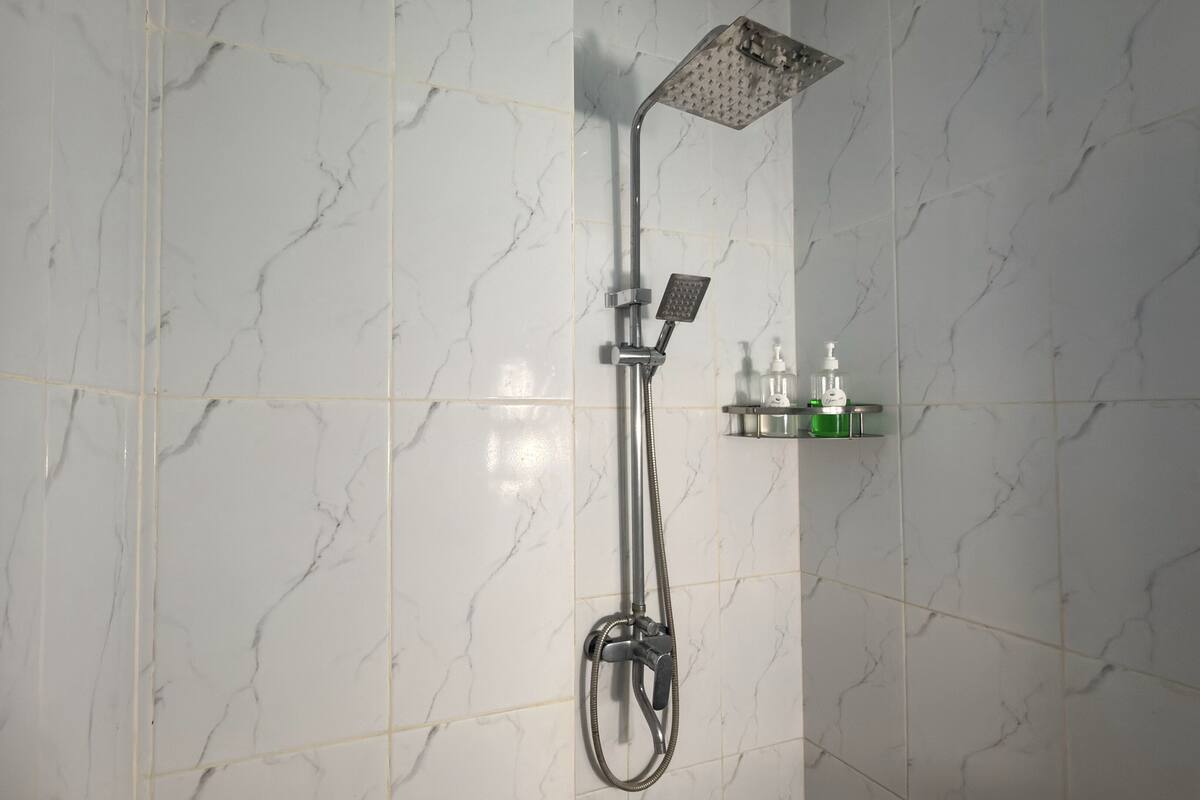 A shower with a handheld showerhead and a wall-mounted control panel.