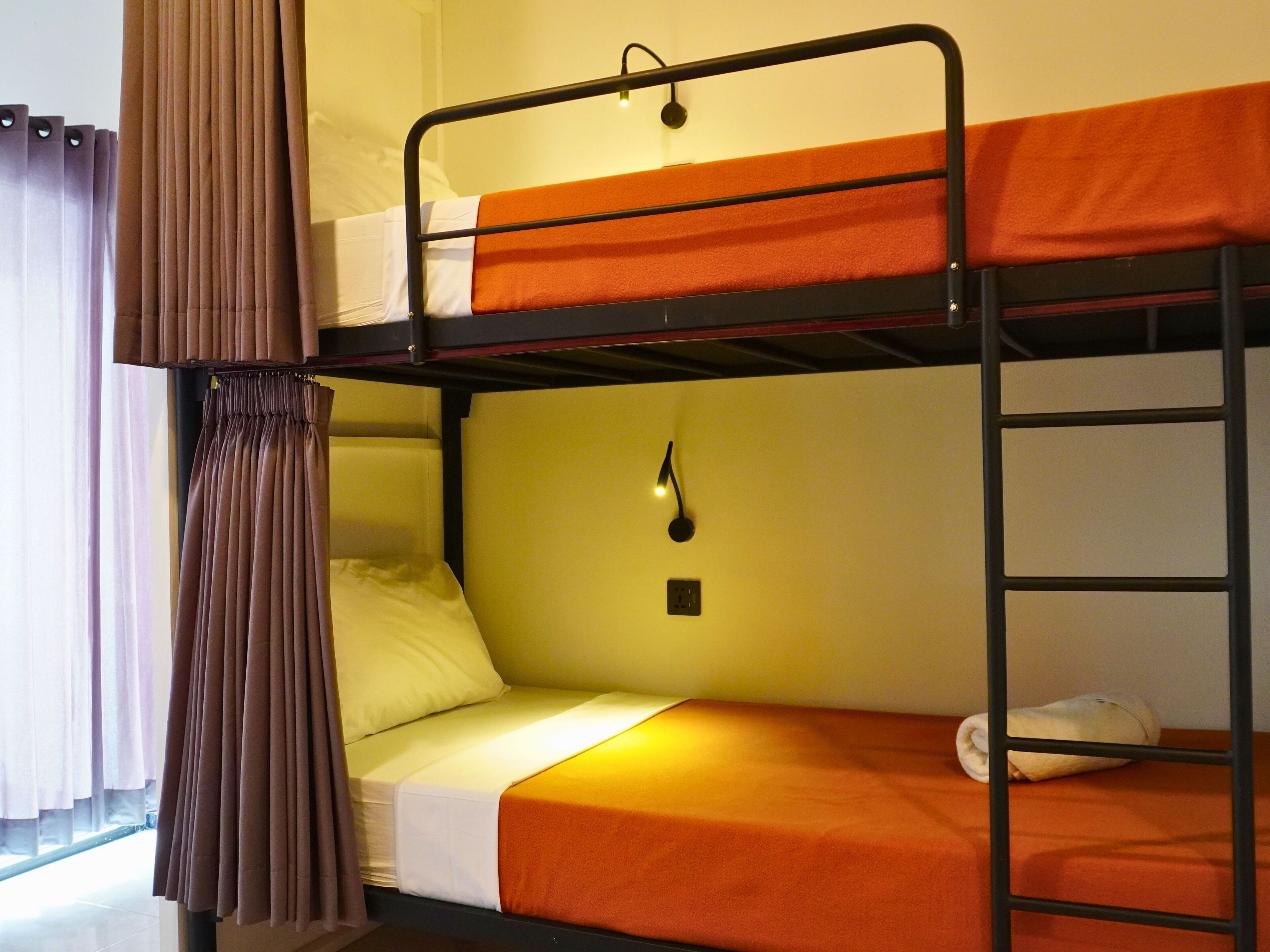 A bunk bed room with orange bedding, a curtain, and a wall-mounted light fixture.