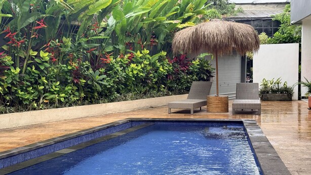 A swimming pool with two wicker chairs and a thatched umbrella. - Summer of Surf Hostel Uluwatu (Ungasan)