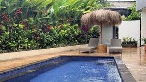 A swimming pool with two wicker chairs and a thatched umbrella. - Summer of Surf Hostel Uluwatu (Ungasan)