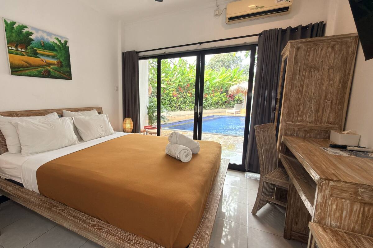 A hotel room with a bed, a desk, a chair, a painting, and a view of an outdoor pool.