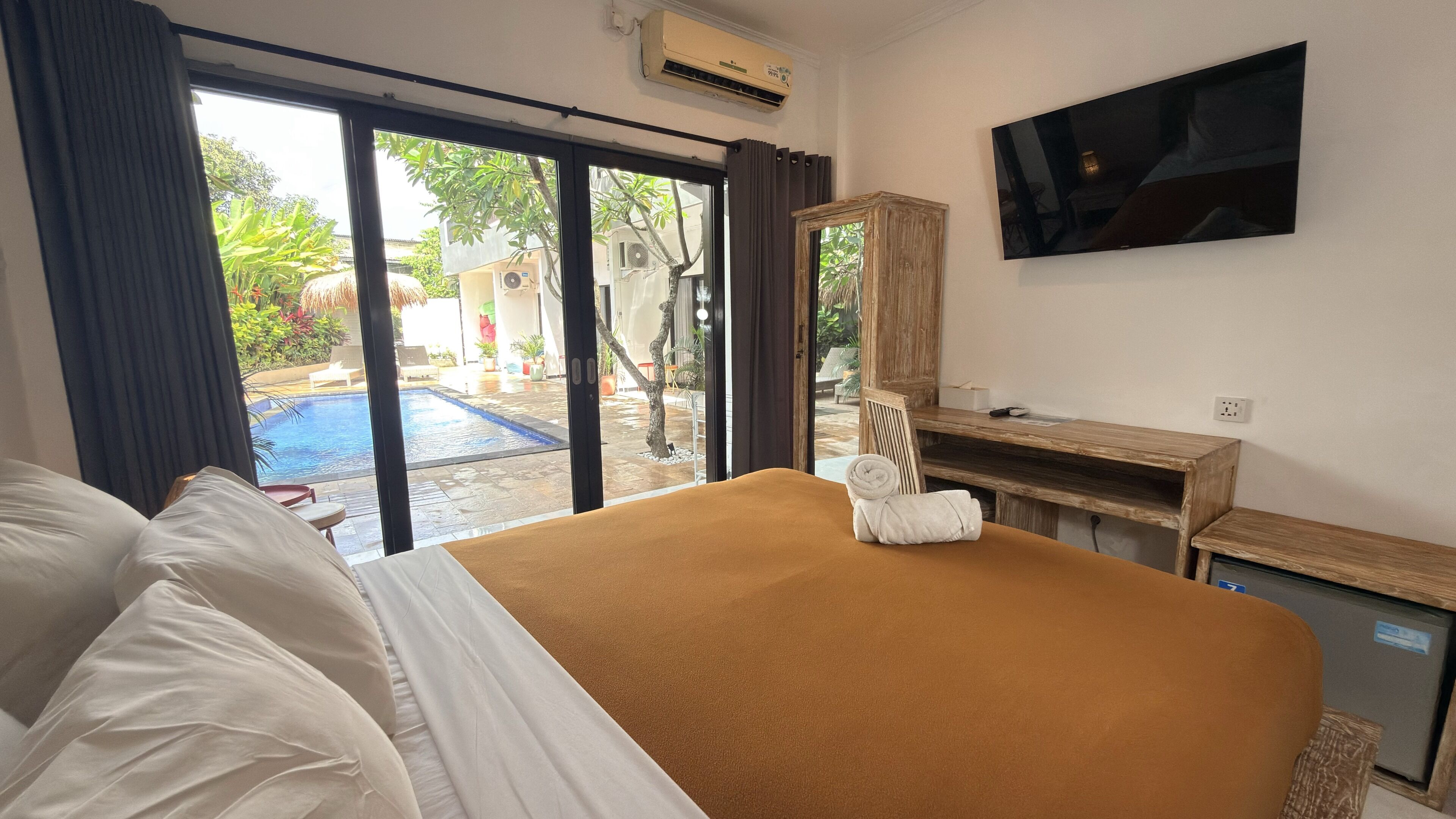 A hotel room with a bed, a TV, a desk, and a view of an outdoor pool area.