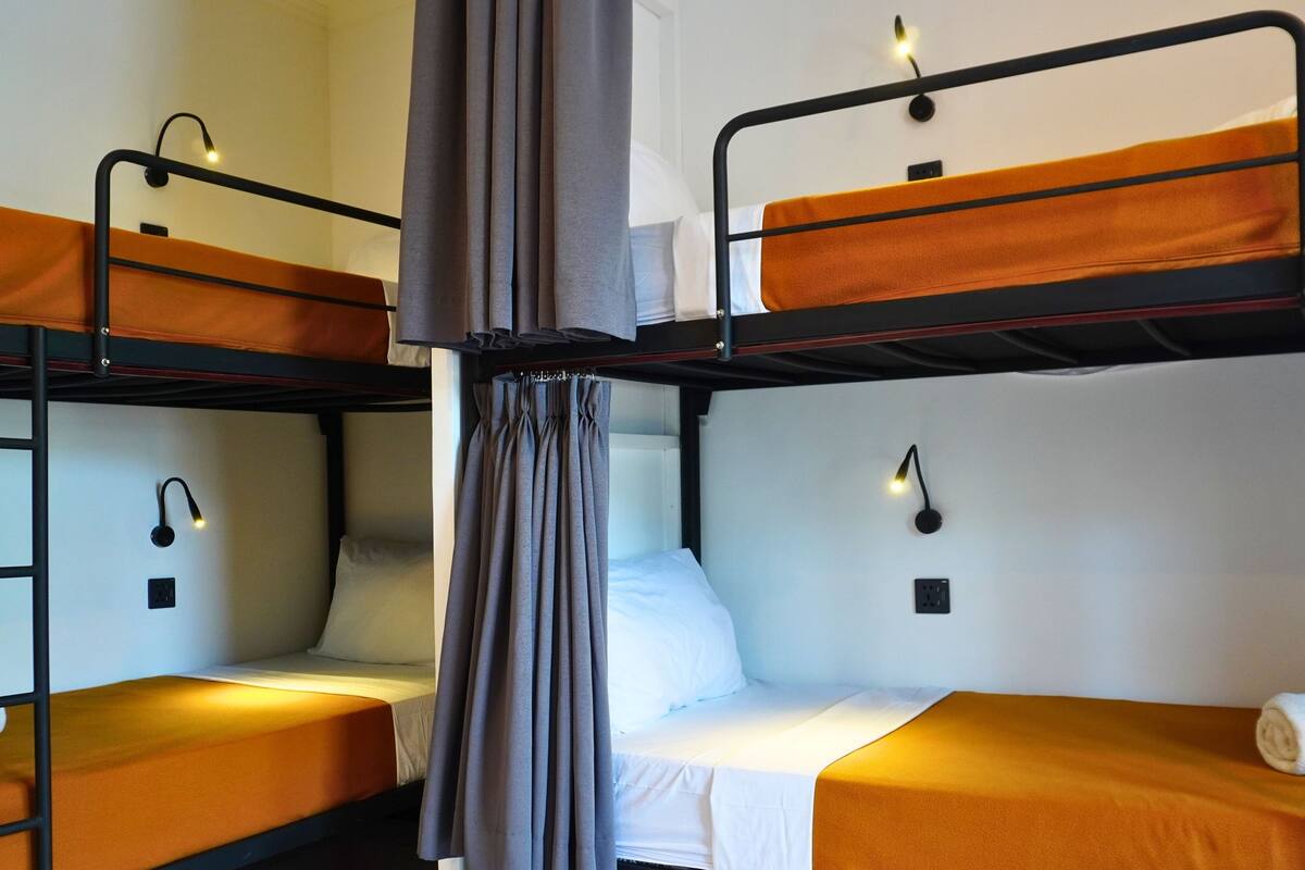 A bunk bed room with two beds, each with a pillow and a blanket. There are wall-mounted lights above each bed.