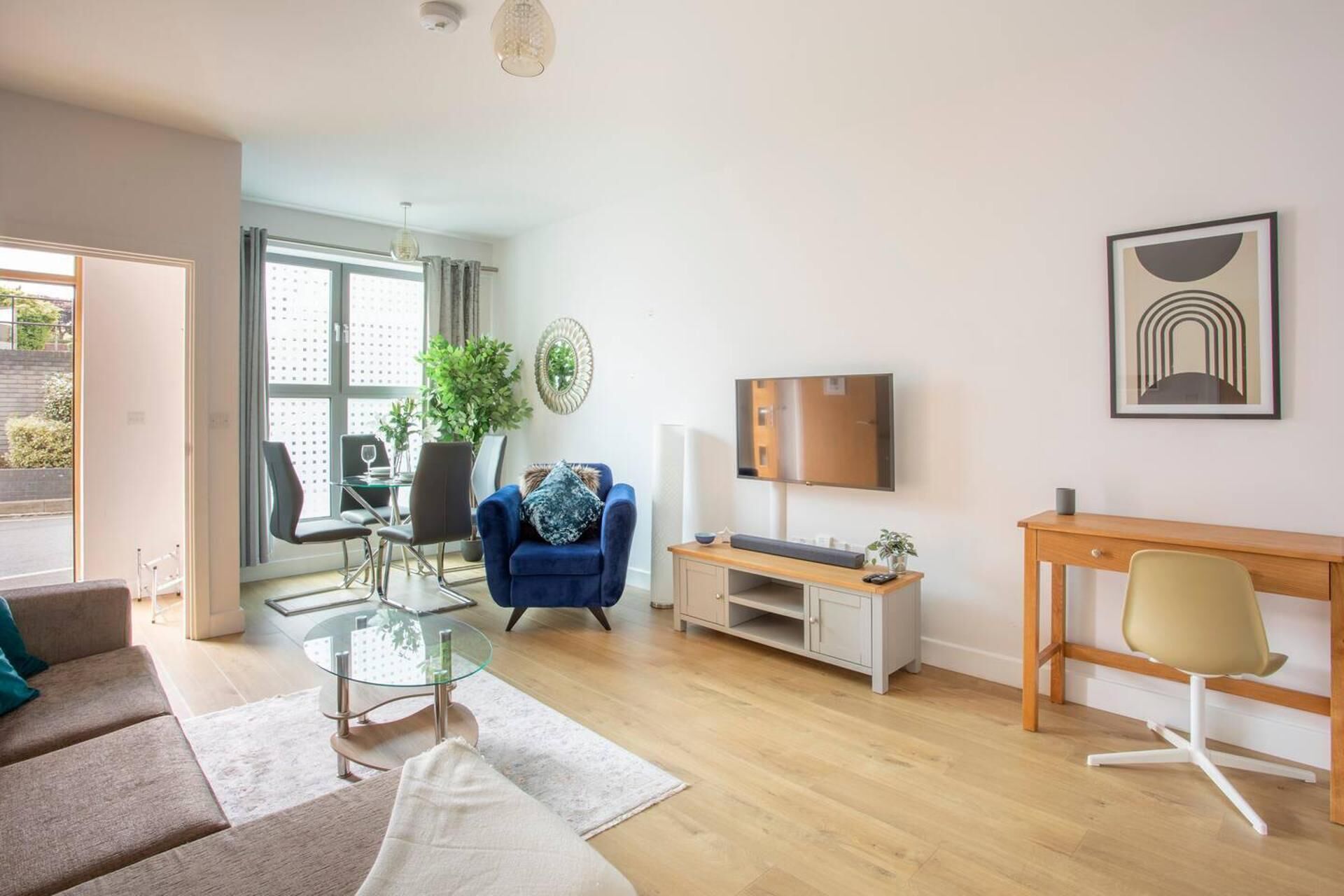 Una sala de estar moderna con un sofá, una mesa de centro de cristal, un televisor, un escritorio y una silla.