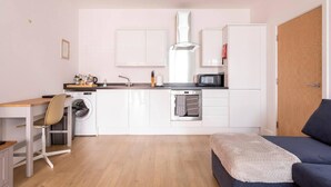 A compact kitchen with a washing machine, microwave, and a small dining area with a chair and table.