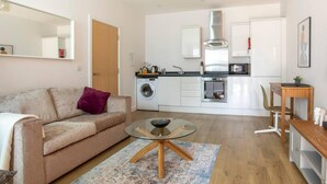 Ett kompakt bostadsutrymme med ett litet kök, en soffa, ett soffbord med glasskiva och en matplats.