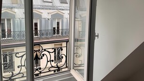 A corner room with a large window overlooking a balcony with ornate iron railings and a view of neighboring buildings. - Spacious Stunning 6th Floor Apartment in Renovated "Haussmannian" Building (Paris)