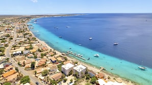Vista aérea de un pueblo costero con un puerto deportivo, edificios a lo largo de la costa y aguas azules cristalinas.