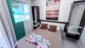 A hotel room with a bed, a window with curtains, a painting on the wall, and a small shelf. - Pousada Ondas do Mar (Ipojuca)