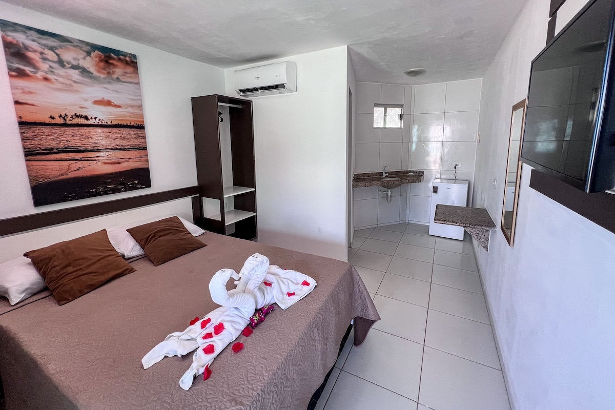 A hotel room with a bed, a wardrobe, a bathroom with a sink and mirror, and a painting on the wall.