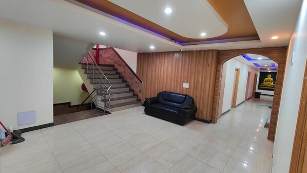A spacious lobby with a staircase, a black leather sofa, and a Buddha statue.
