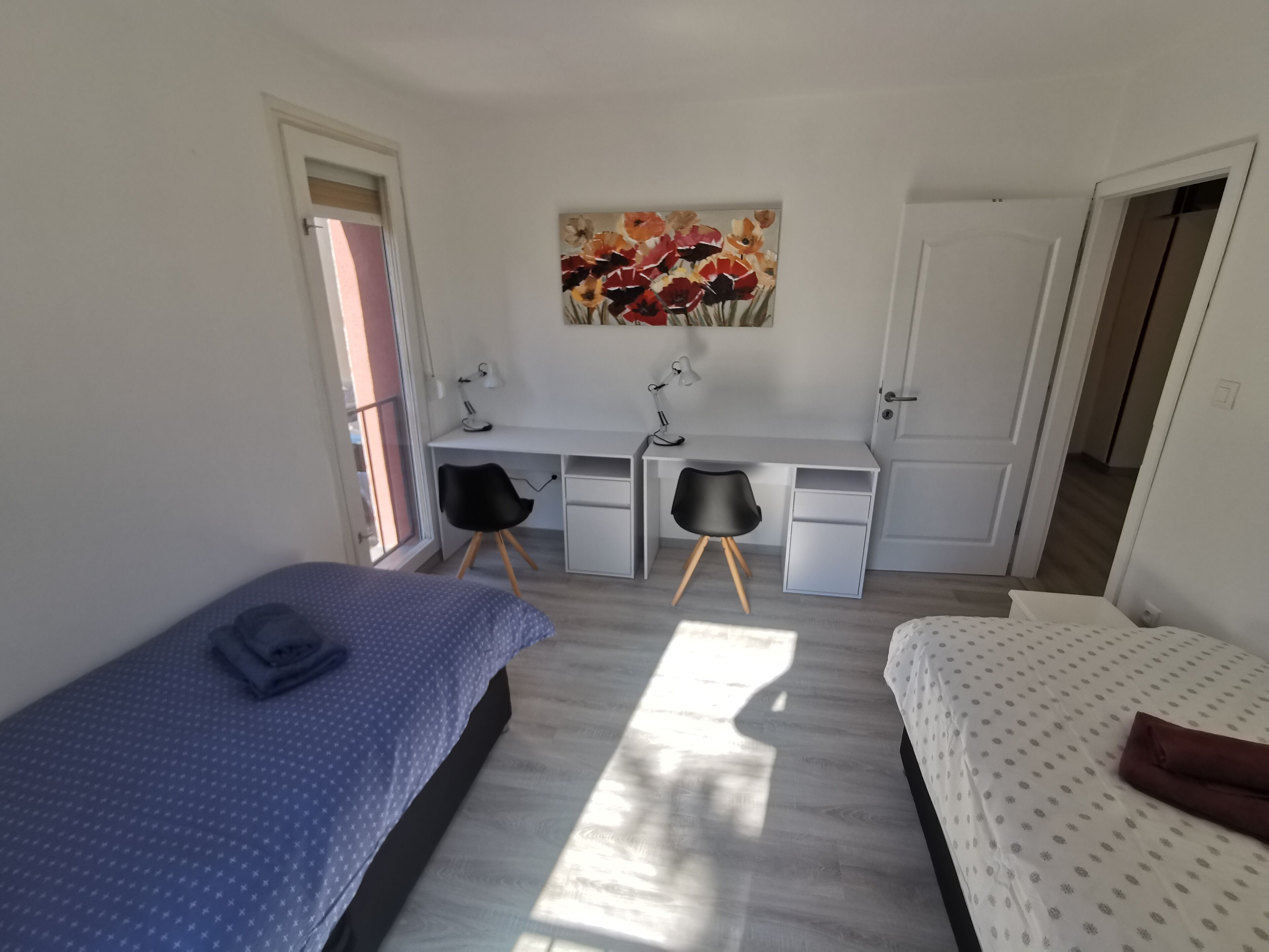 A bedroom with a bed, a desk, two chairs, and a painting on the wall.