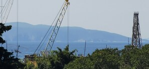 Blick auf die Küste mit Bergen im Hintergrund, einem Kran und einem Sendeturm.