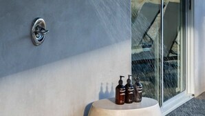A modern outdoor area with a glass door leading to a patio, a wall-mounted shower, and a small seating area with bottles. - Sunset Heights By Homestead Modern (Joshua Tree)