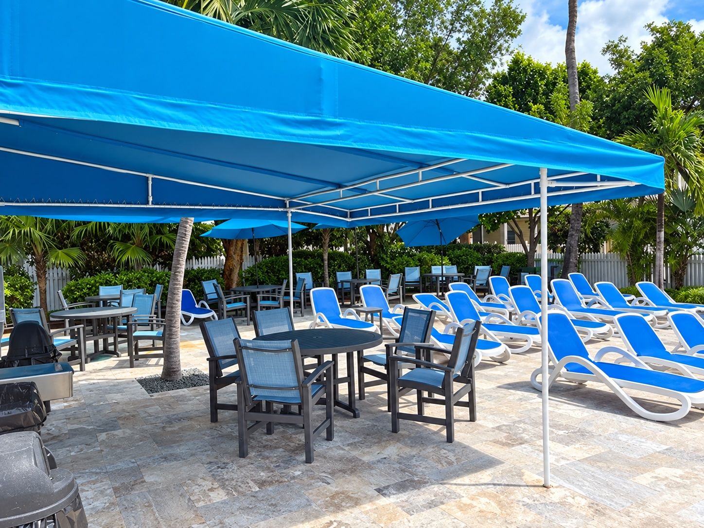 Un área junto a la piscina con sillones de descanso y mesas bajo sombrillas azules.