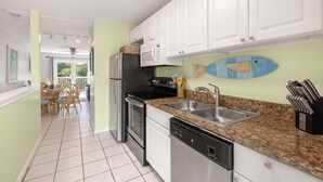 A modern kitchen with white cabinets, a granite countertop, stainless steel appliances, and a view to the outside. - THE PELICAN PEARL ~ Charming 2 BR/1 Ba Condo in Truman Annex! (Key West)