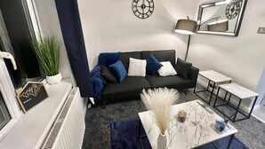 A modern living room with a black sofa, a white coffee table, and a floor lamp. - Beautiful 2-bed House in Watford (Watford)