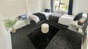 A modern bedroom with two beds, a desk, a laptop, and a large window with curtains. - Beautiful 2-bed House in Watford (Watford)