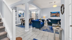 A spacious living area with a blue sofa, a dining table with chairs, and a kitchen in the background. - Stylish 6 bedroom! Near Disney! with private pool! (Kissimmee)