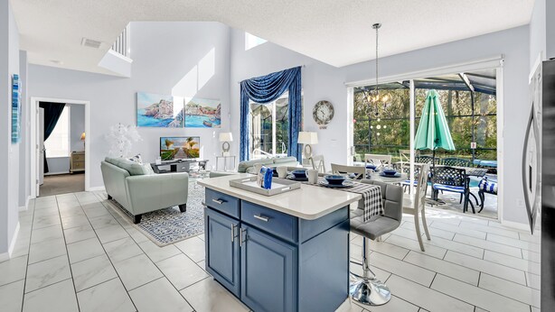 A modern kitchen with a central island, a dining area with outdoor seating, and a living room with a sofa and coffee table. - Stylish 6 bedroom! Near Disney! with private pool! (Kissimmee)