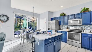 A modern kitchen with blue cabinets, stainless steel appliances, and a dining area with a view. - Stylish 6 bedroom! Near Disney! with private pool! (Kissimmee)