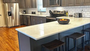 Une cuisine moderne dotée d’un grand îlot central, d’appareils électroménagers en acier inoxydable et de tabourets de bar en bois foncé.