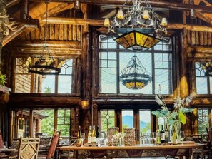 A rustic wooden interior with large windows, a chandelier, and a dining table set with glasses and bottles. - Beautiful 3-bedroom suite located in the Whiteface lodge in Lake Placid NY (Lake Placid)