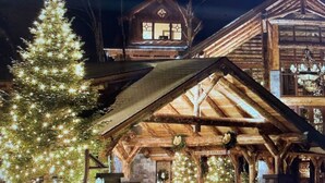 Un chalet en rondins dont le toit est recouvert de neige, un sapin de Noël illuminé et une pancarte indiquant « Entrée du chalet ».