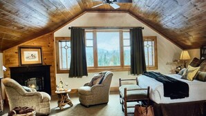 Une chambre confortable située dans les combles, avec une cheminée, un grand lit et une vue sur l’extérieur par une fenêtre.