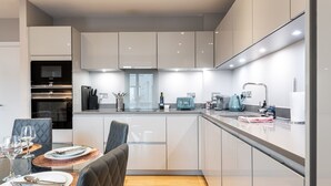 A modern kitchen with white cabinets, a built-in oven, and a dining area with a table set for two.