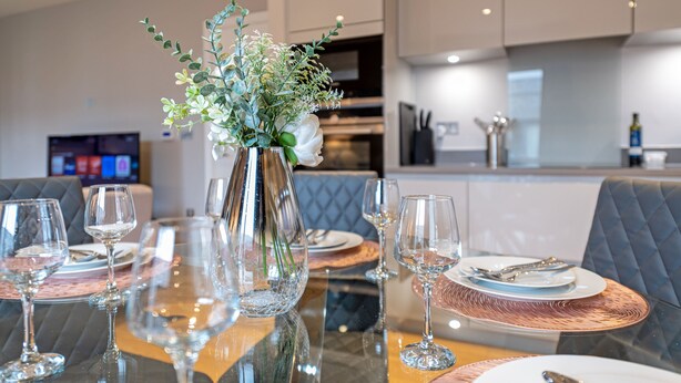 A dining table set with wine glasses, plates, and cutlery, with a vase of flowers in the center.