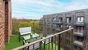 A balcony with a green lawn, a white table and chairs, and a view of a modern building with balconies.