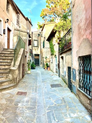 Un estrecho callejón empedrado entre edificios, con una escalera a la izquierda y una entrada porticada a la derecha.