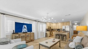 A modern living room with a sofa, coffee table, and a TV. There is a kitchen area with a dining table and chairs.