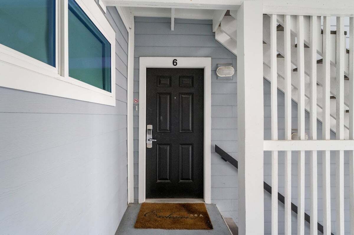 A black door with the number 6, a white exterior wall, and a white staircase with vertical railings.
