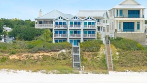A beachfront property with a multi-story building, a staircase leading to the beach, and a view of the ocean.