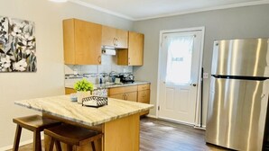 A kitchen with wooden cabinets, a marble countertop, a stainless steel refrigerator, and a door with a window. - Farm living by Santos Trails & the Villages! (Summerfield)