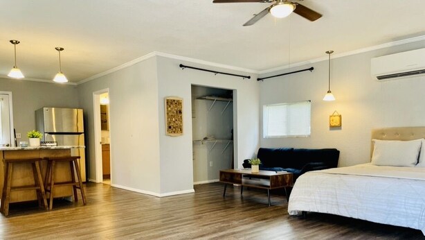 A compact bedroom with a bed, a desk, and a chair. There is a ceiling fan and a window with blinds. - Farm living by Santos Trails & the Villages! (Summerfield)