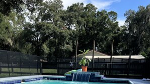 A swimming pool with a waterfall feature, surrounded by a fence and trees. - Farm living by Santos Trails & the Villages! (Summerfield)