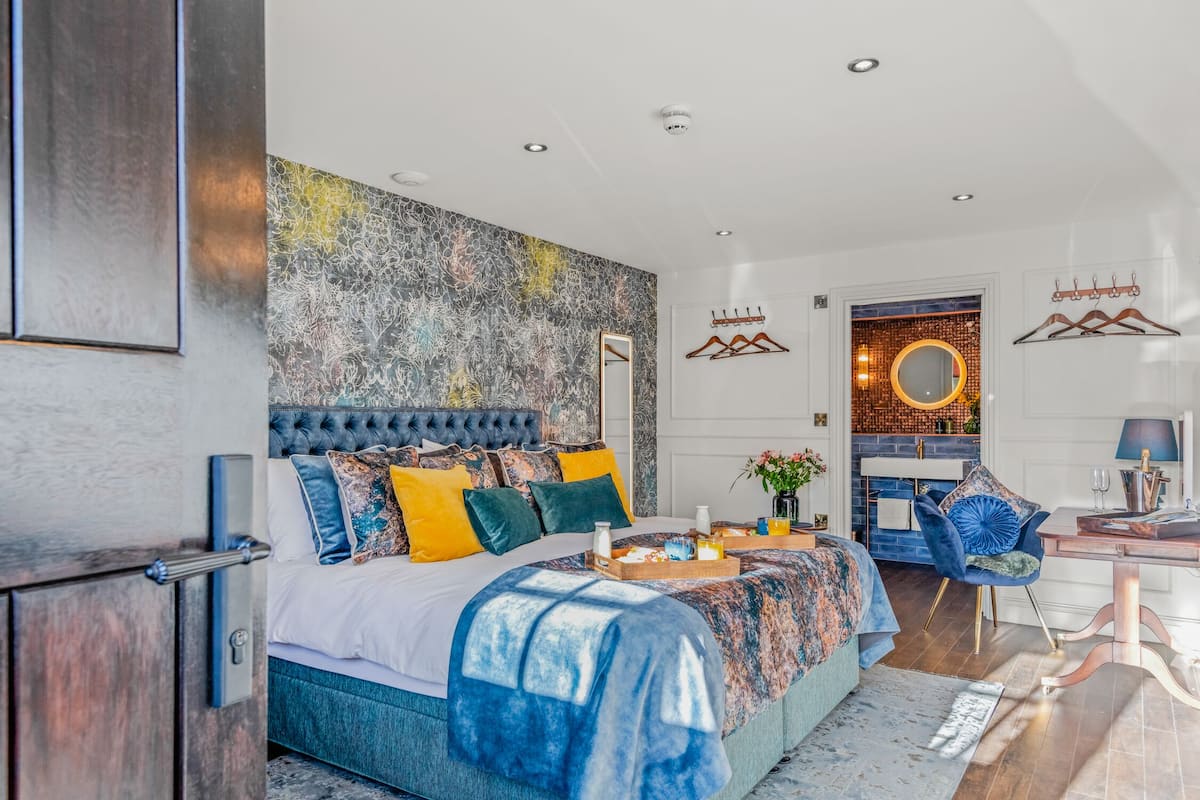 Quarto moderno com cama grande, escrivaninha e banheiro visível por uma porta aberta.