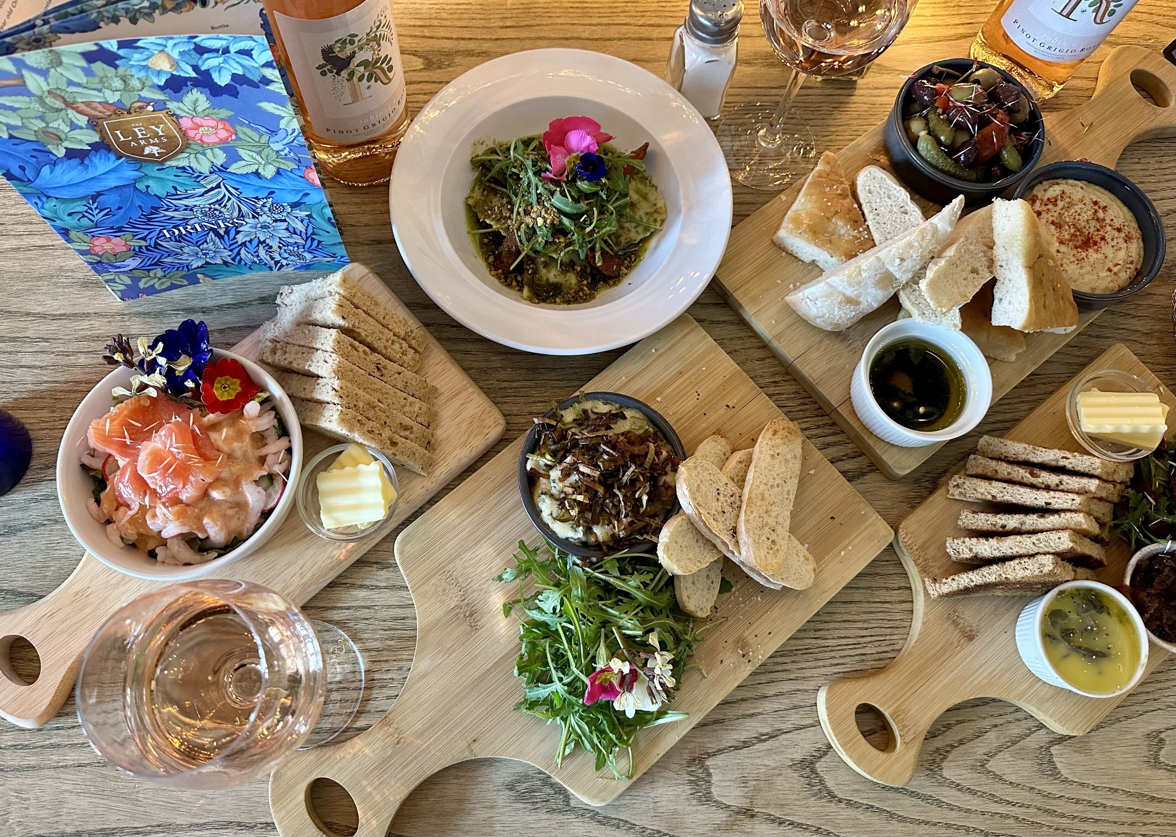 Una mesa de madera con diferentes alimentos, como un bol de salmón, pan y una botella de vino.