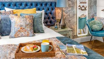 A bedroom with a tufted headboard, a bedside table with a lamp, a chair, and a tray with breakfast.