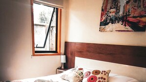 A neatly made bed with a patterned blanket, a pillow with a floral design, and a towel rolled up.