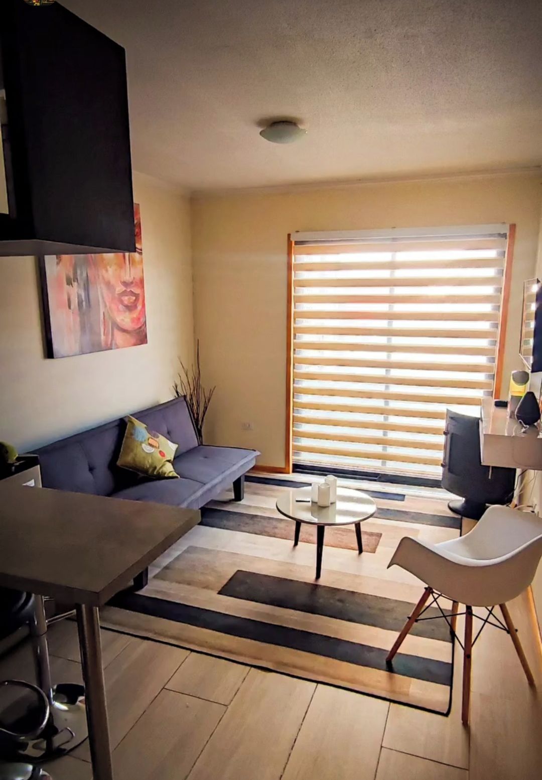 A living room with a sofa, a coffee table, a dining table, and a large window with blinds.