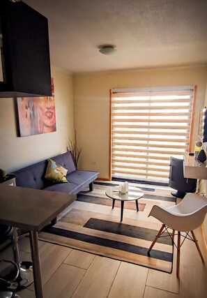 A living room with a sofa, a coffee table, a dining table, and a large window with blinds.