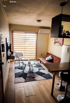 A compact hotel room with a sofa, a dining table, a coffee table, and a patterned rug.