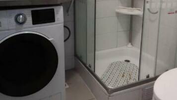 A compact bathroom with a glass-enclosed shower, a washing machine, and a toilet.